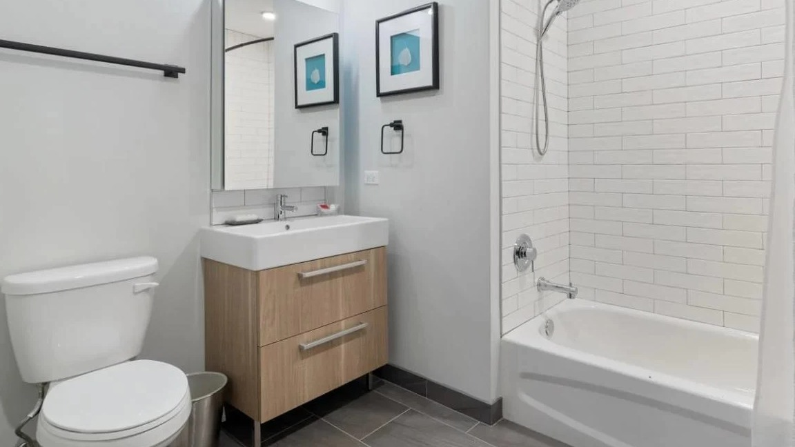 Contemporary bathroom with a light wood vanity, toilet, and a combined shower-tub with white subway tiles at Millennium on LaSalle in Chicago