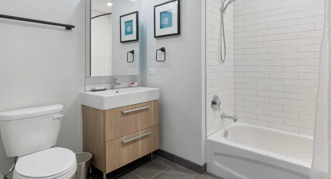 Contemporary bathroom with a light wood vanity, toilet, and a combined shower-tub with white subway tiles at Millennium on LaSalle in Chicago