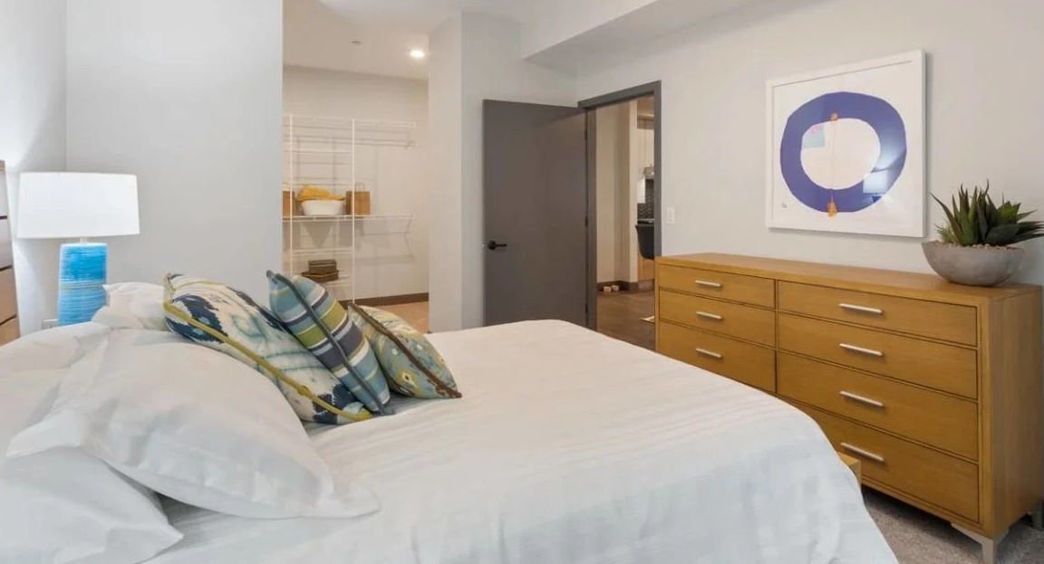 Cozy bedroom with a wooden bed frame, large dresser, and an open walk-in closet with ample shelving at Millennium on LaSalle in Chicago