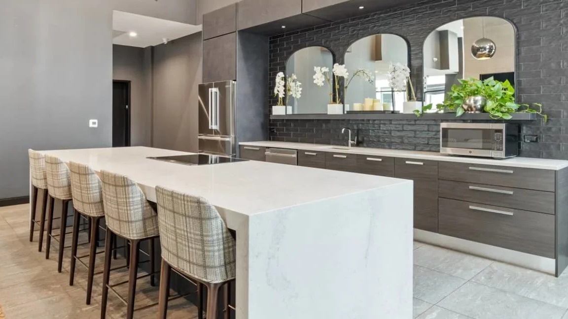 High-ceilinged chef's kitchen with dark cabinetry, stainless steel appliances, and an expansive white island with seating at Millennium on LaSalle in Chicago