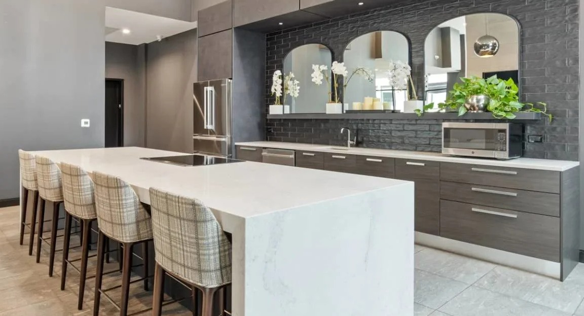 High-ceilinged chef's kitchen with dark cabinetry, stainless steel appliances, and an expansive white island with seating at Millennium on LaSalle in Chicago