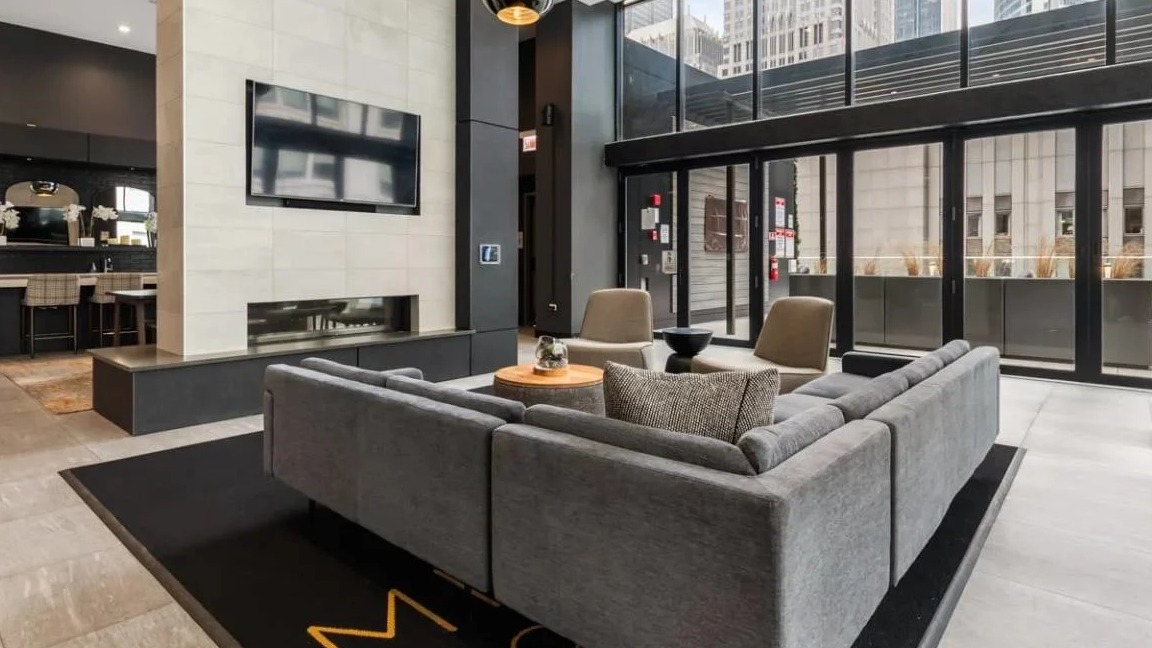 Grand main lounge with a sleek fireplace, large TV, comfortable sectional sofa, and floor-to-ceiling windows at Millennium on LaSalle in Chicago