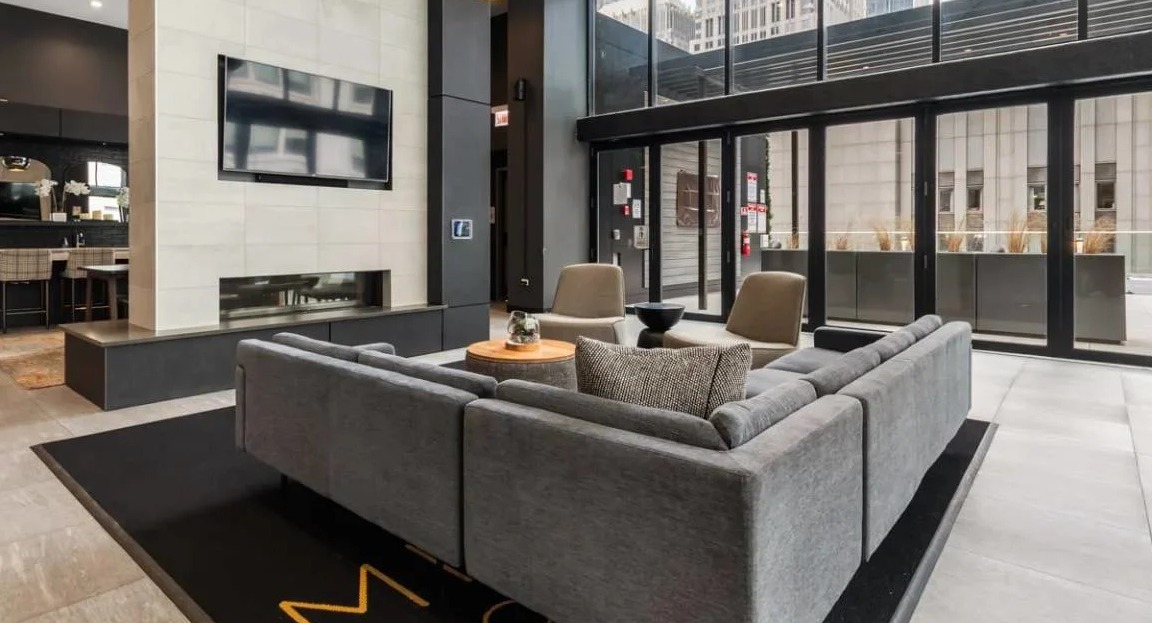 Grand main lounge with a sleek fireplace, large TV, comfortable sectional sofa, and floor-to-ceiling windows at Millennium on LaSalle in Chicago