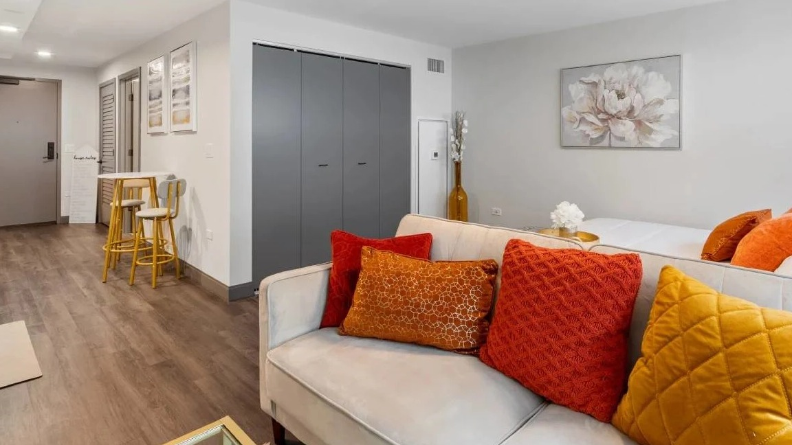 Compact studio apartment living area with a sofa, colorful pillows, and a small dining nook at Millennium on LaSalle in Chicago