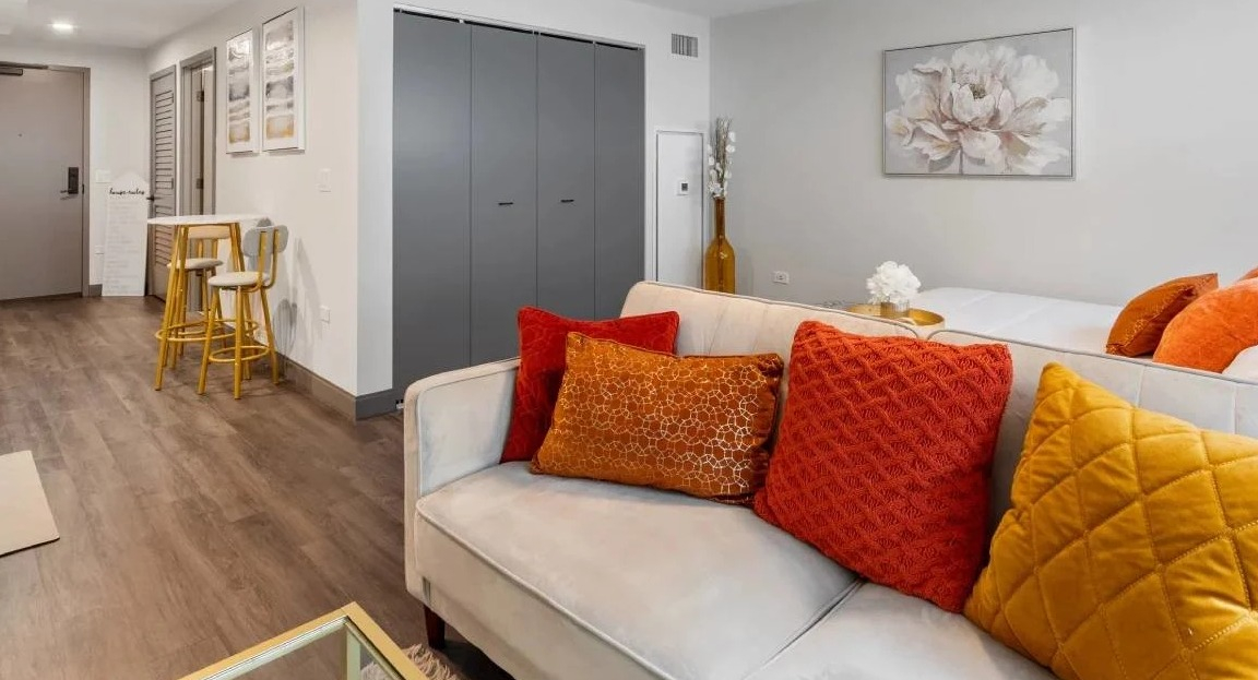 Compact studio apartment living area with a sofa, colorful pillows, and a small dining nook at Millennium on LaSalle in Chicago