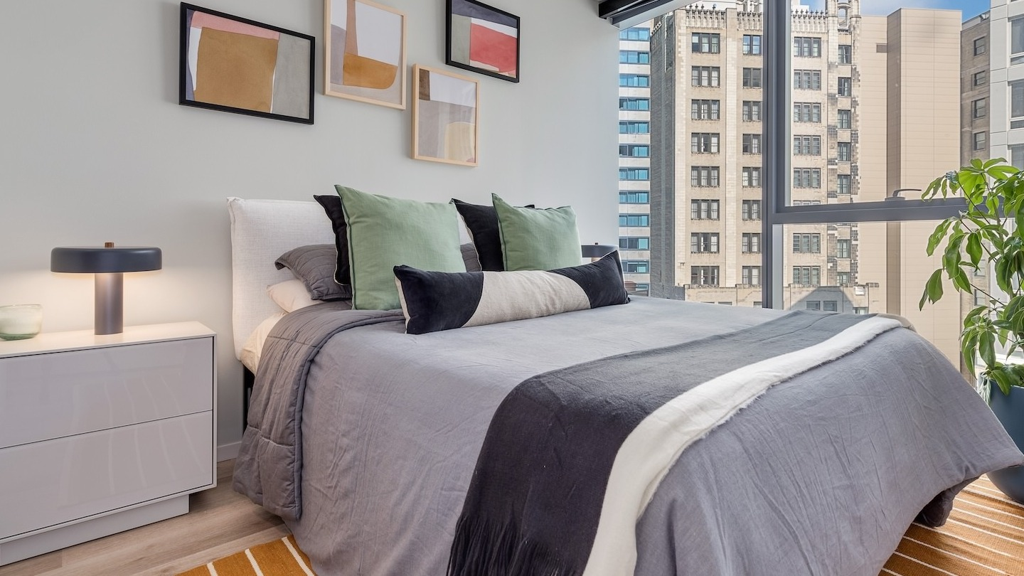 Contemporary bedroom with a comfortable bed, colorful accents, and large windows offering city views at Millie on Michigan Chicago