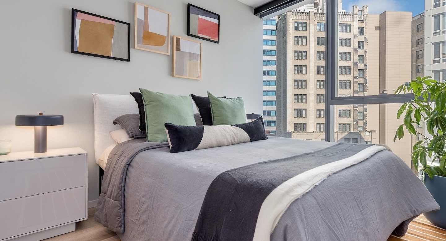 Contemporary bedroom with a comfortable bed, colorful accents, and large windows offering city views at Millie on Michigan Chicago