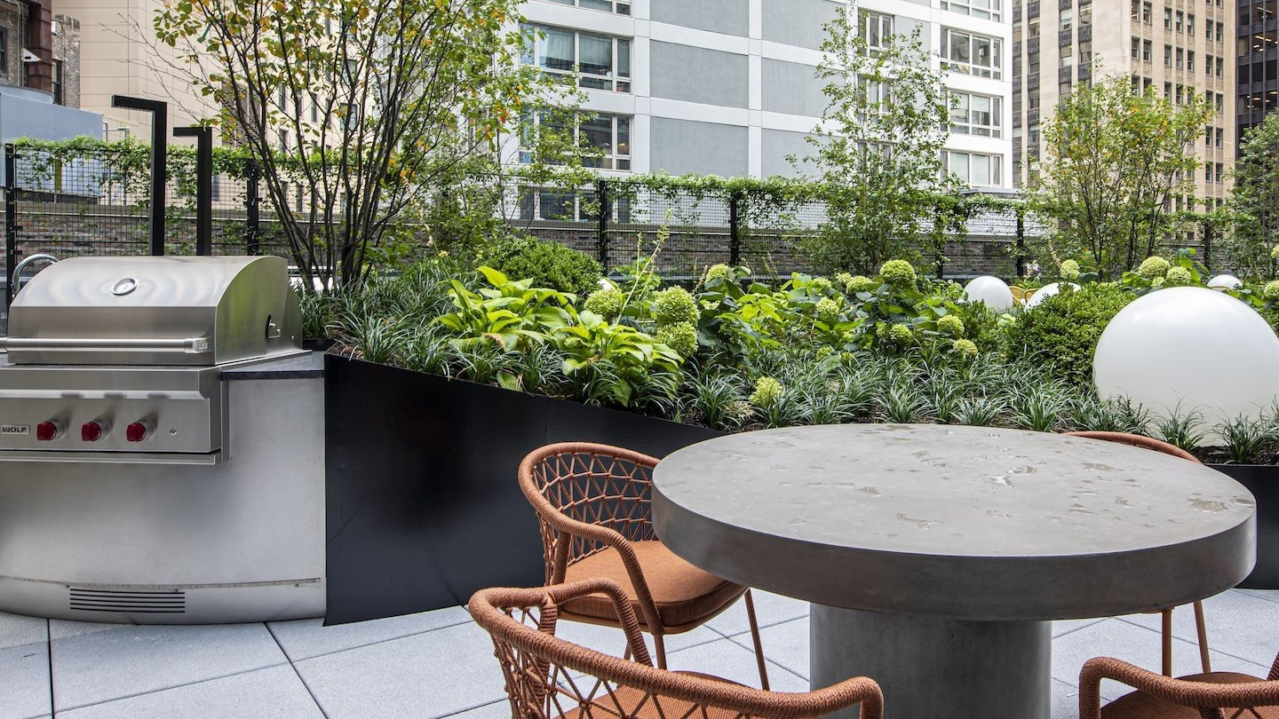 Outdoor patio area with a grill, seating, and lush greenery at Millie on Michigan apartments in Chicago