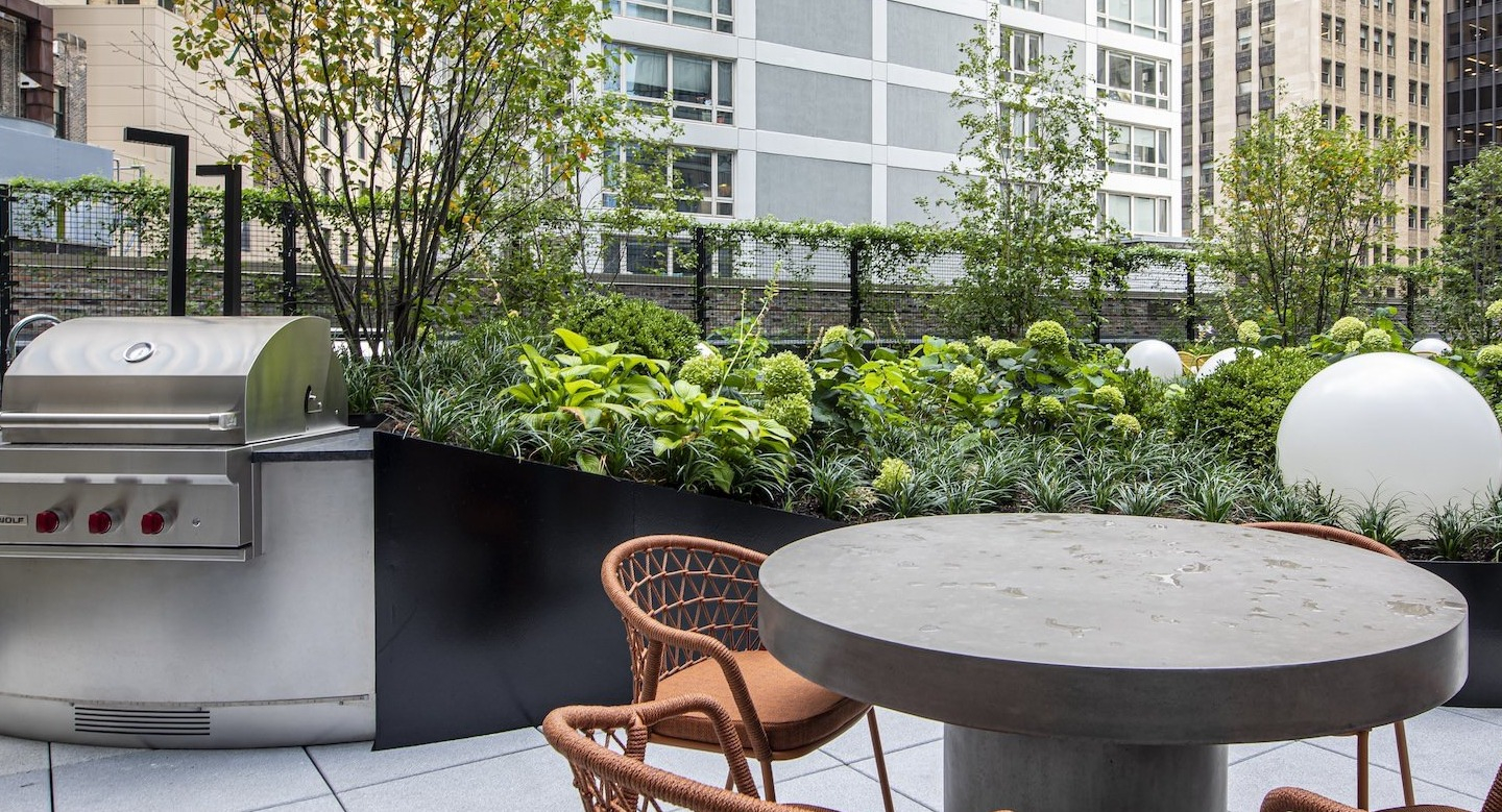 Outdoor patio area with a grill, seating, and lush greenery at Millie on Michigan apartments in Chicago