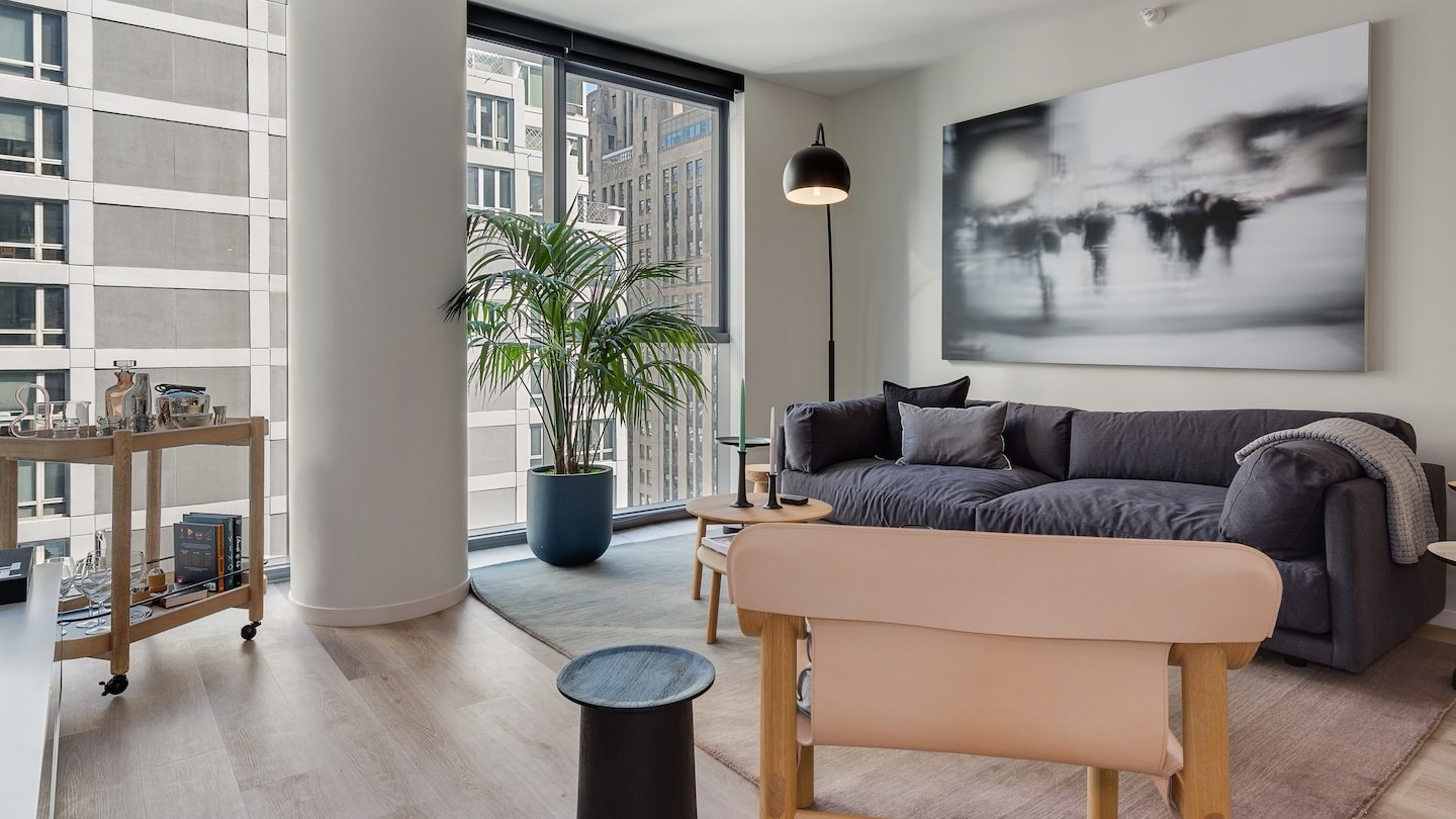 Stylish living area with a dark sofa, modern artwork, and expansive city views from large windows at Millie on Michigan Chicago