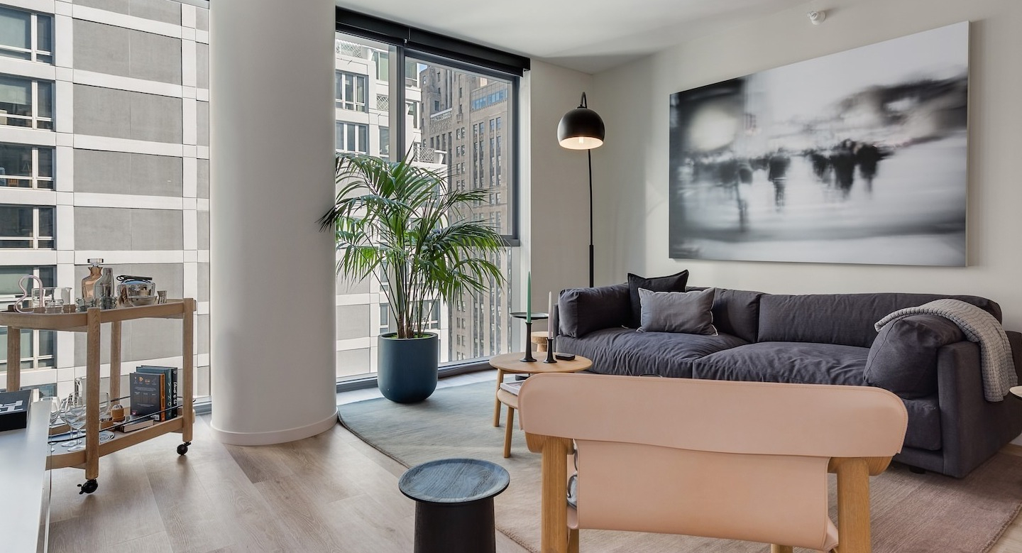 Stylish living area with a dark sofa, modern artwork, and expansive city views from large windows at Millie on Michigan Chicago