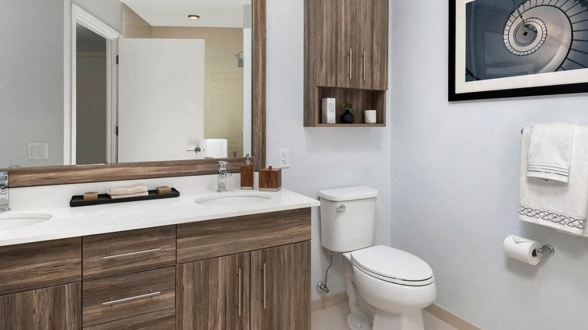 Modern bathroom featuring a double vanity with wood cabinets, a large mirror, and a framed spiral art piece at Moment Apartments in Chicago