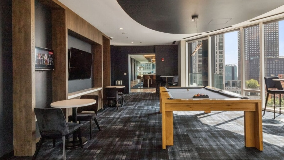 A chic game room at Moment Apartments in Chicago, featuring a modern pool table, seating areas, and city views