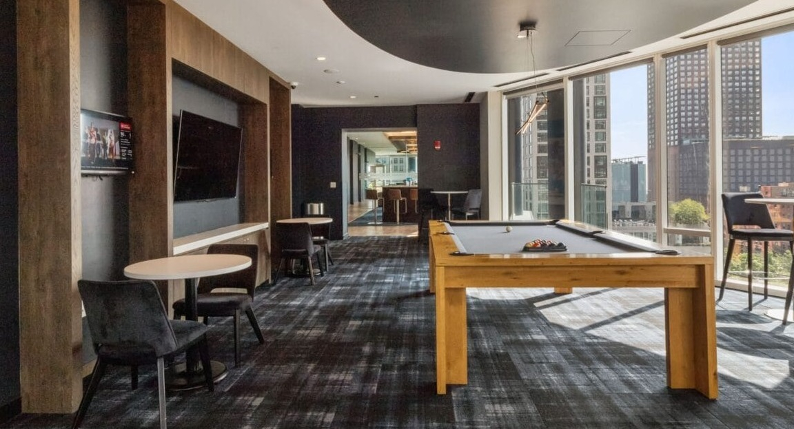 A chic game room at Moment Apartments in Chicago, featuring a modern pool table, seating areas, and city views
