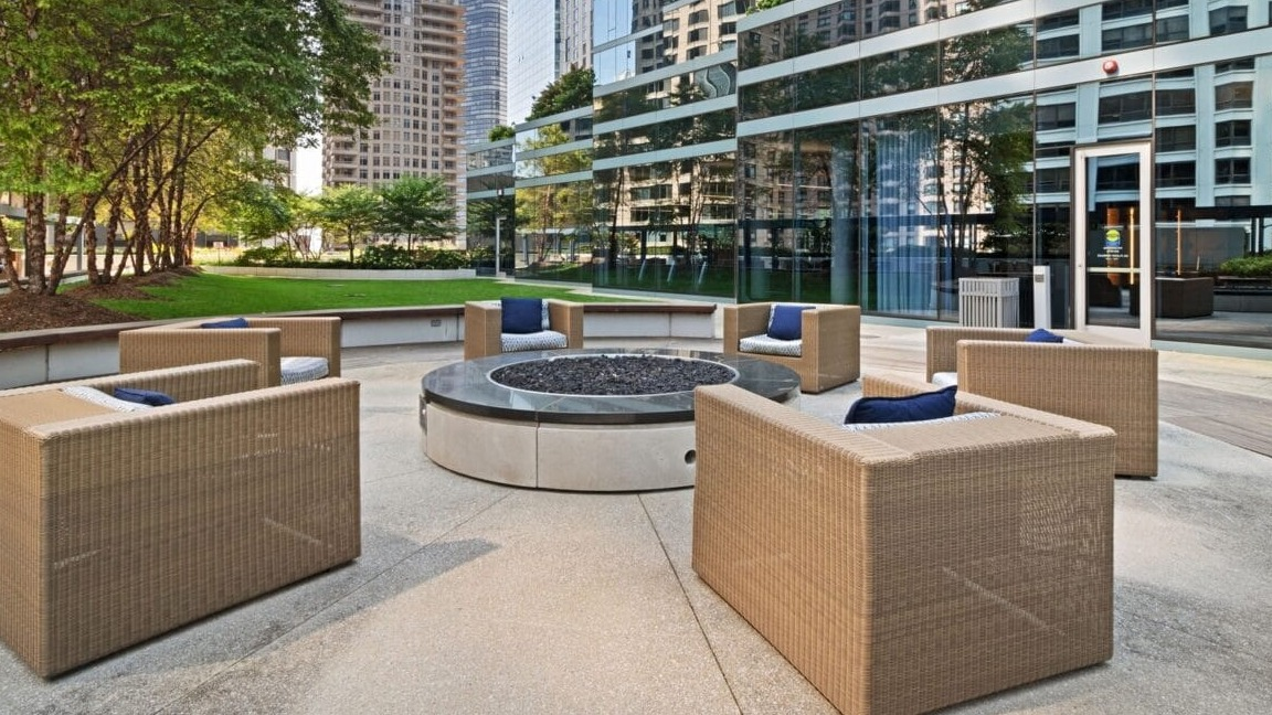 Inviting outdoor fire pit lounge at Moment Apartments in Chicago, with comfortable seating surrounded by trees and modern buildings
