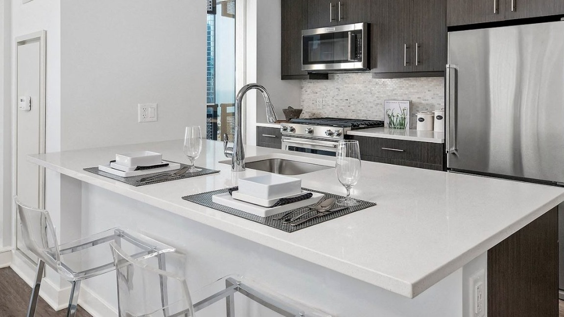 Sleek apartment kitchen at Moment Apartments in Chicago, with dark cabinetry, stainless steel appliances, a large island, and stylish pendant lights