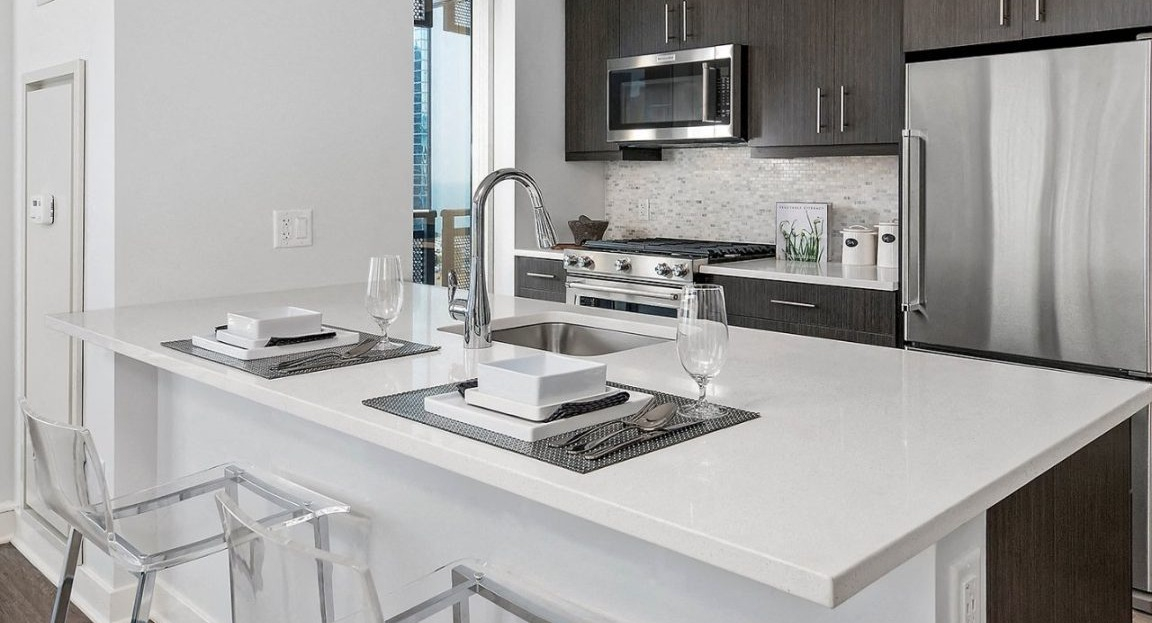 Sleek apartment kitchen at Moment Apartments in Chicago, with dark cabinetry, stainless steel appliances, a large island, and stylish pendant lights