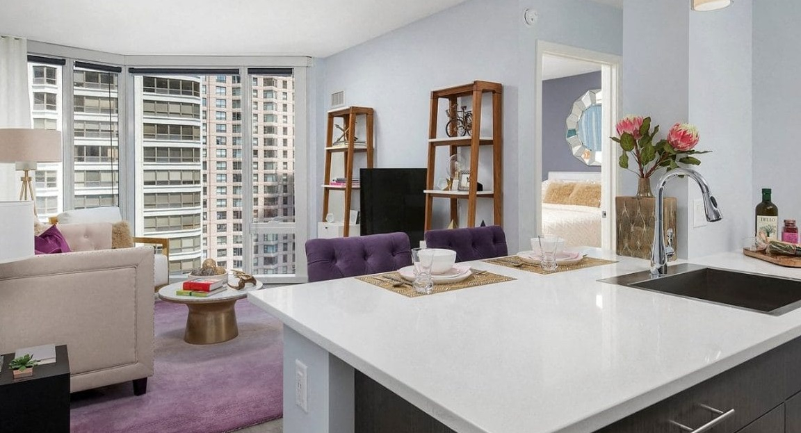 Open-concept kitchen and living area at Moment Apartments in Chicago, featuring a white quartz island, purple accents, and city views