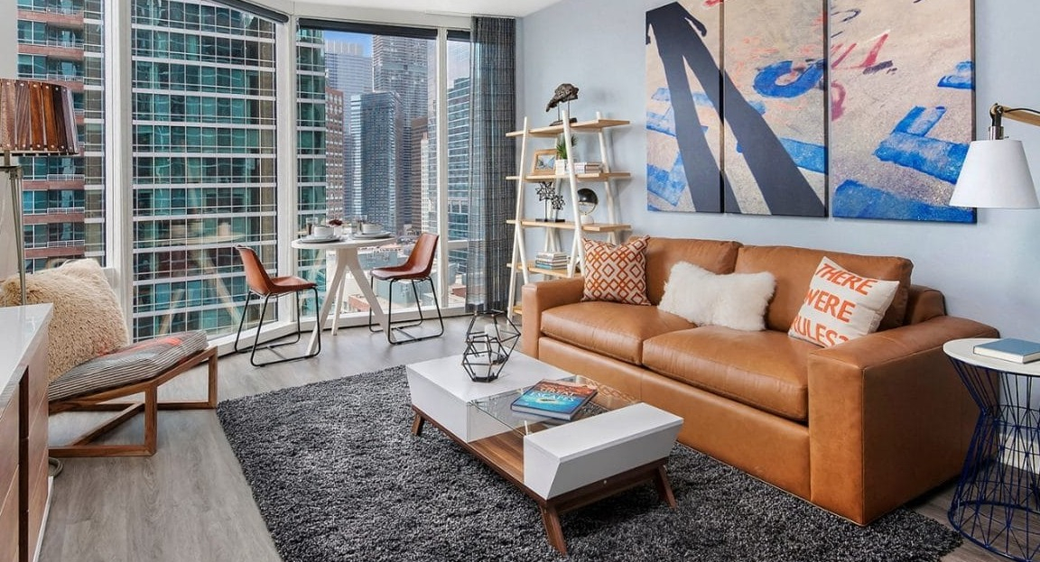 Urban loft-style living room with a leather sofa, industrial-chic coffee table, and large windows with city skyline views at Moment Apartments in Chicago
