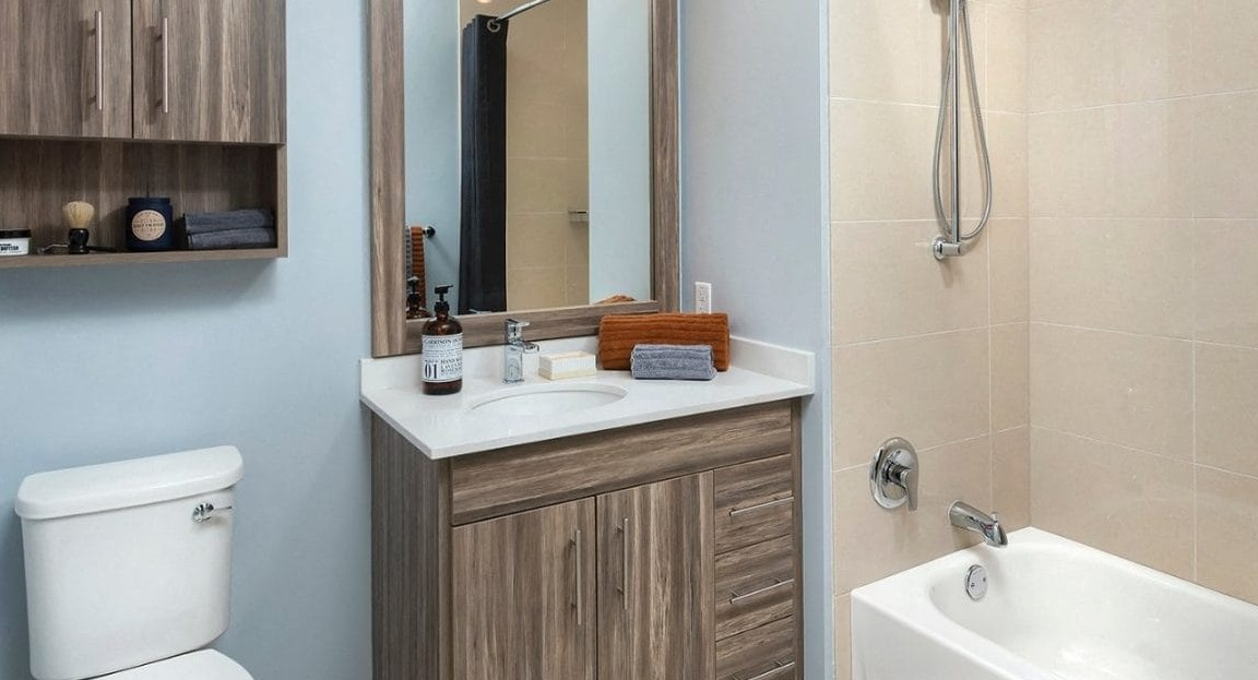 Modern apartment bathroom at Moment Apartments in Chicago, featuring a wood-grain vanity, stylish mirror, and a bathtub with a shower