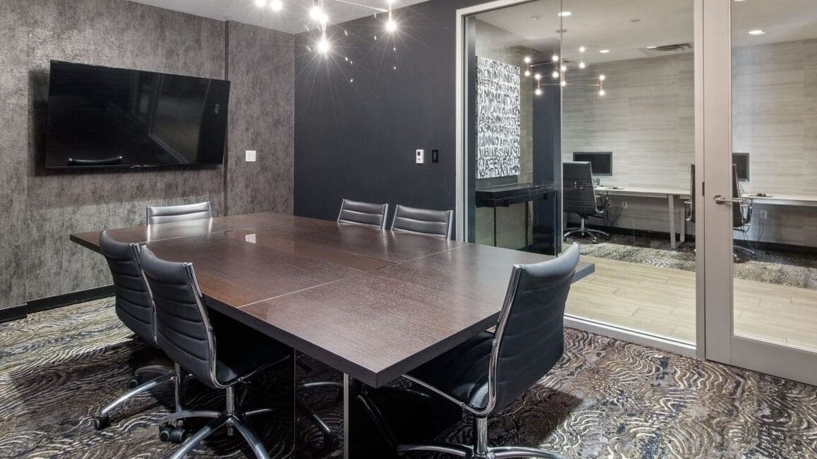 A modern conference room with a large table, executive chairs, and an adjoining private office at Moment Apartments in Chicago