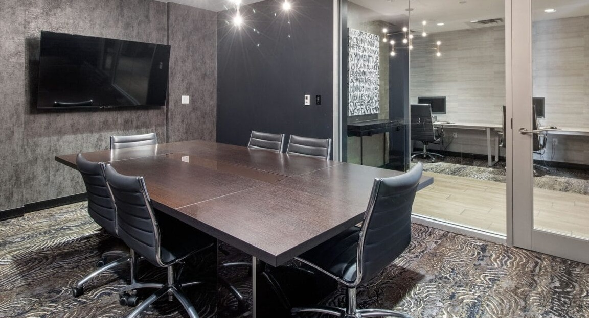 A modern conference room with a large table, executive chairs, and an adjoining private office at Moment Apartments in Chicago