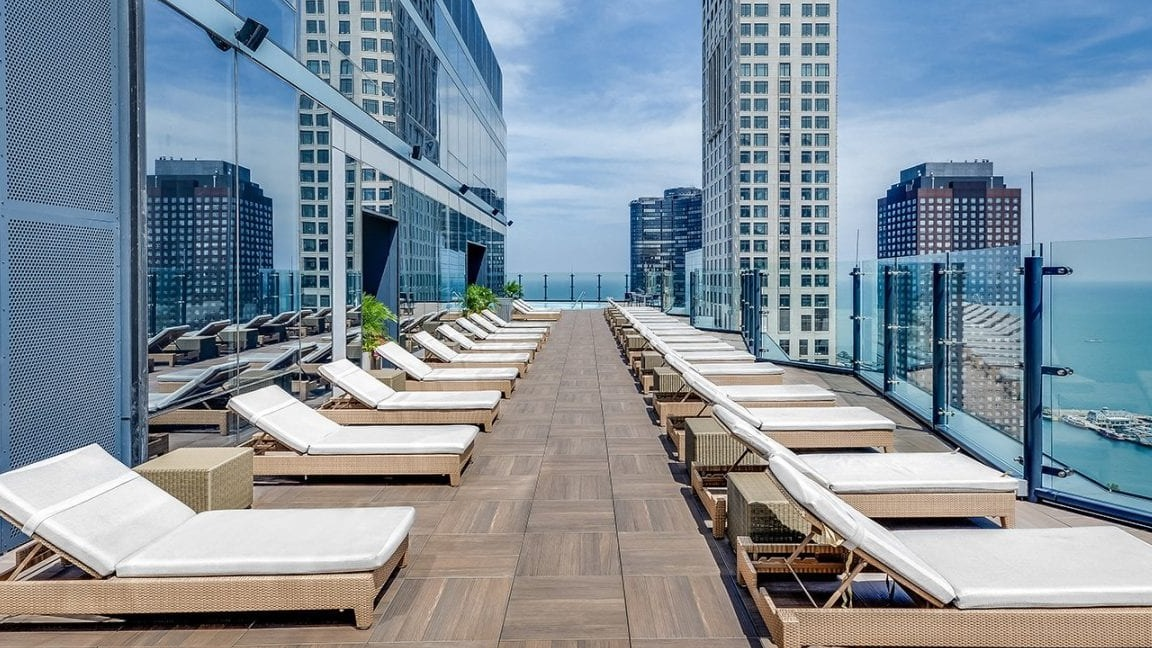 Luxurious rooftop sun deck at Moment Apartments in Chicago, lined with lounge chairs and offering breathtaking views of the lake and city skyline