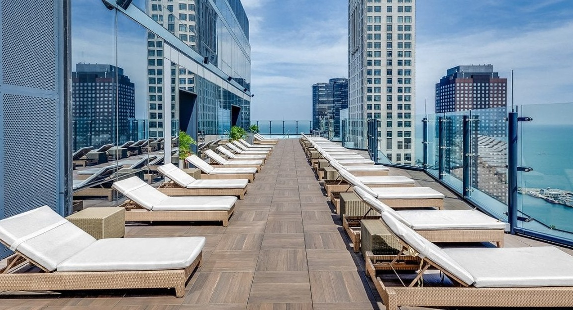 Luxurious rooftop sun deck at Moment Apartments in Chicago, lined with lounge chairs and offering breathtaking views of the lake and city skyline