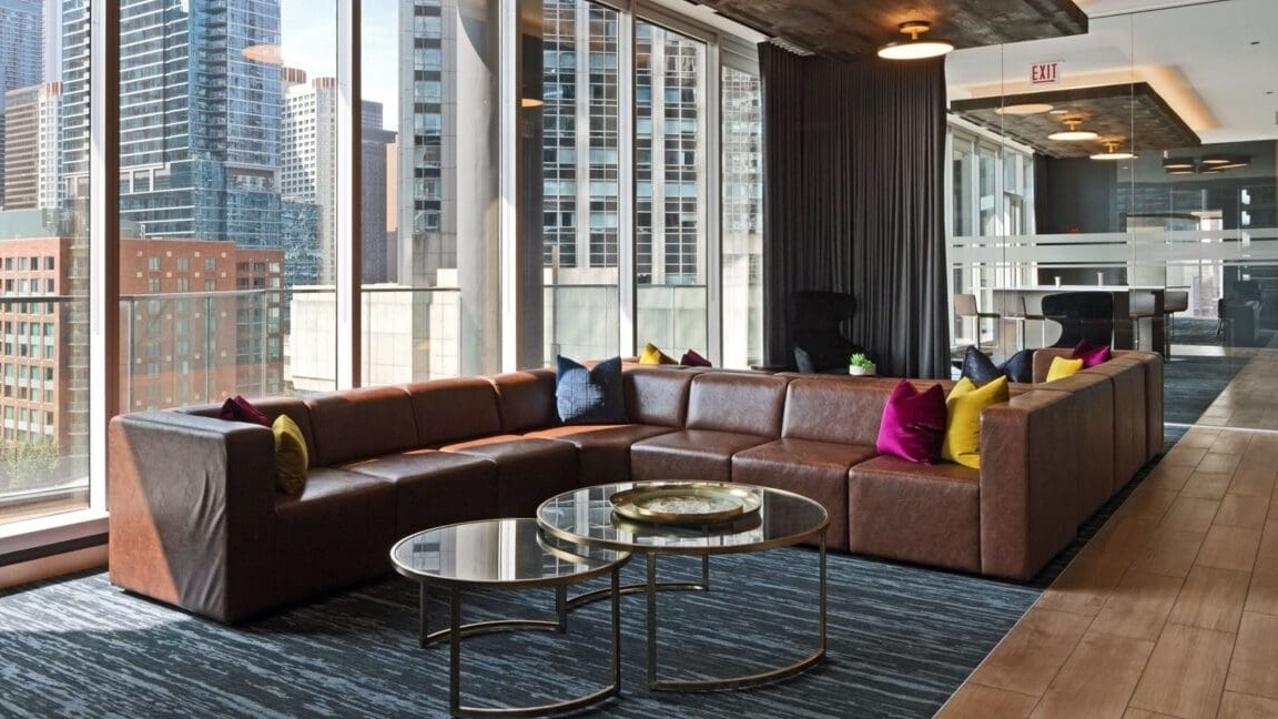 A spacious and inviting lounge area with a large leather sectional sofa and city views at Moment Apartments in Chicago