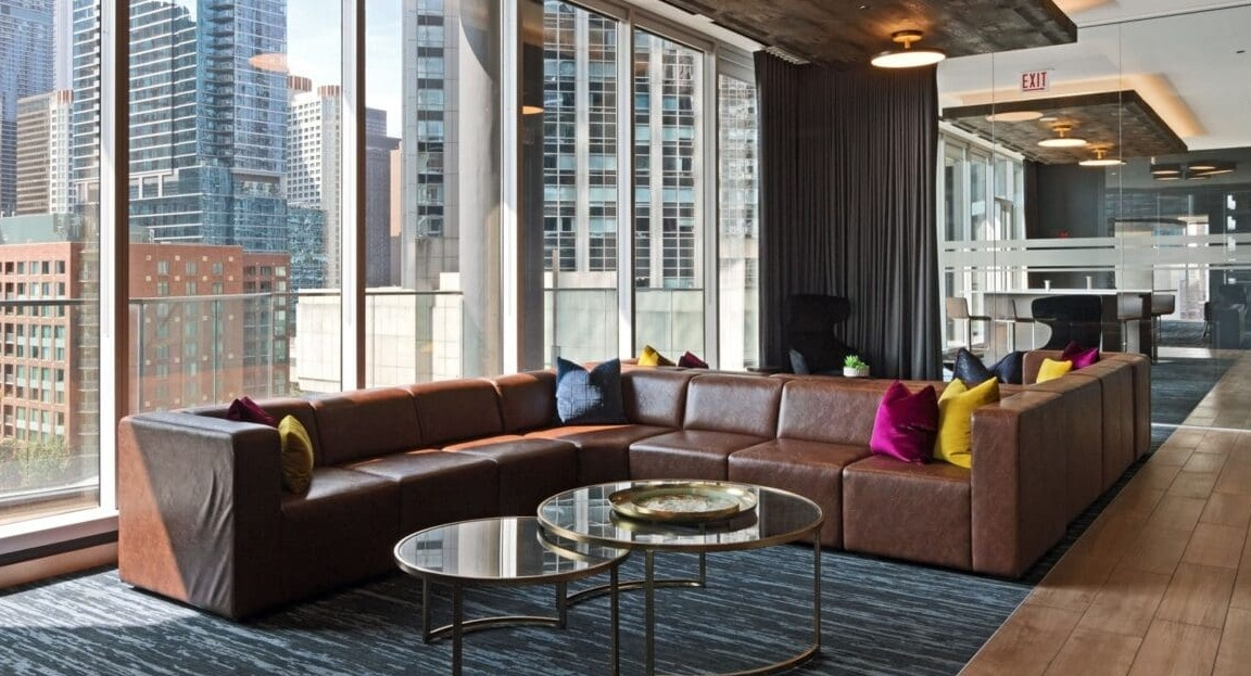 A spacious and inviting lounge area with a large leather sectional sofa and city views at Moment Apartments in Chicago