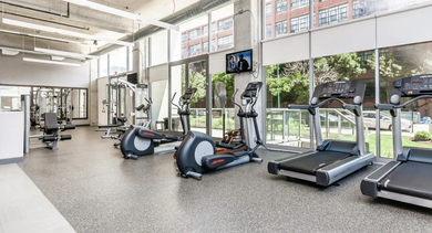 Bright fitness center with cardio machines, including treadmills and ellipticals, and large windows at Mondial River West in Chicago