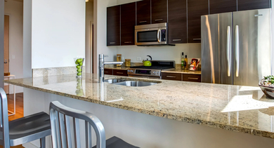 Modern kitchen with granite countertops, stainless steel appliances, and a breakfast bar with two stools at Mondial River West in Chicago