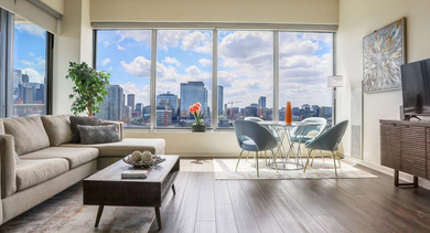 Open-concept living room with a comfortable sectional sofa, dining area, and stunning city views from large windows at Mondial River West in Chicago