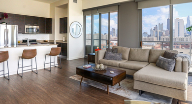 Modern open-layout kitchen and living area featuring a breakfast bar with stools and a spacious sectional sofa at Mondial River West in Chicago
