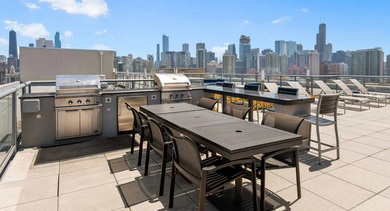 Rooftop outdoor grilling and dining area with multiple barbecues, tables, and lounge chairs, overlooking the Chicago skyline at Mondial River West