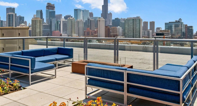 Rooftop lounge with comfortable blue sofas, a fire pit, and a spectacular Chicago skyline view on a sunny day at Mondial River West