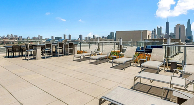 Expansive rooftop sundeck featuring numerous lounge chairs for sunbathing, with panoramic city views at Mondial River West in Chicago