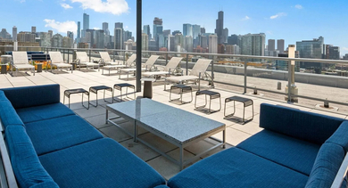 Covered rooftop terrace seating area with large blue sofas and incredible views of the Chicago skyline at Mondial River West