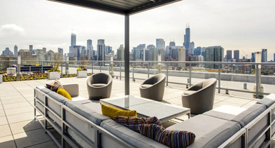 Chic rooftop terrace featuring a gray sectional sofa, modern chairs, and an impressive backdrop of the Chicago skyline at Mondial River West