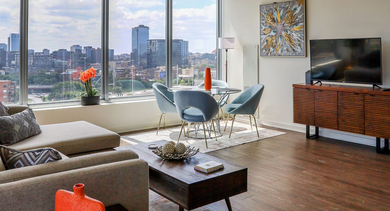 Spacious living room with a sectional sofa, elegant dining table, and a wide view of the Chicago cityscape at Mondial River West