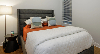 Cozy apartment bedroom at Monroe Aberdeen Place in Chicago, featuring a comfortable bed with colorful bedding and a stylish bedside lamp