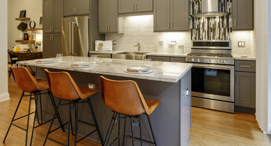 Gourmet apartment kitchen at Monroe Aberdeen Place in Chicago, featuring a large island with bar seating, stainless steel appliances, and sleek cabinetry