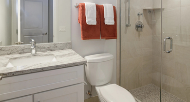 Modern apartment bathroom at Monroe Aberdeen Place in Chicago, featuring a sleek vanity, granite countertop, and a spacious glass-enclosed shower