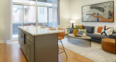 Bright open-concept living area at Monroe Aberdeen Place in Chicago, featuring a modern kitchen island, comfortable sofa, and a private balcony