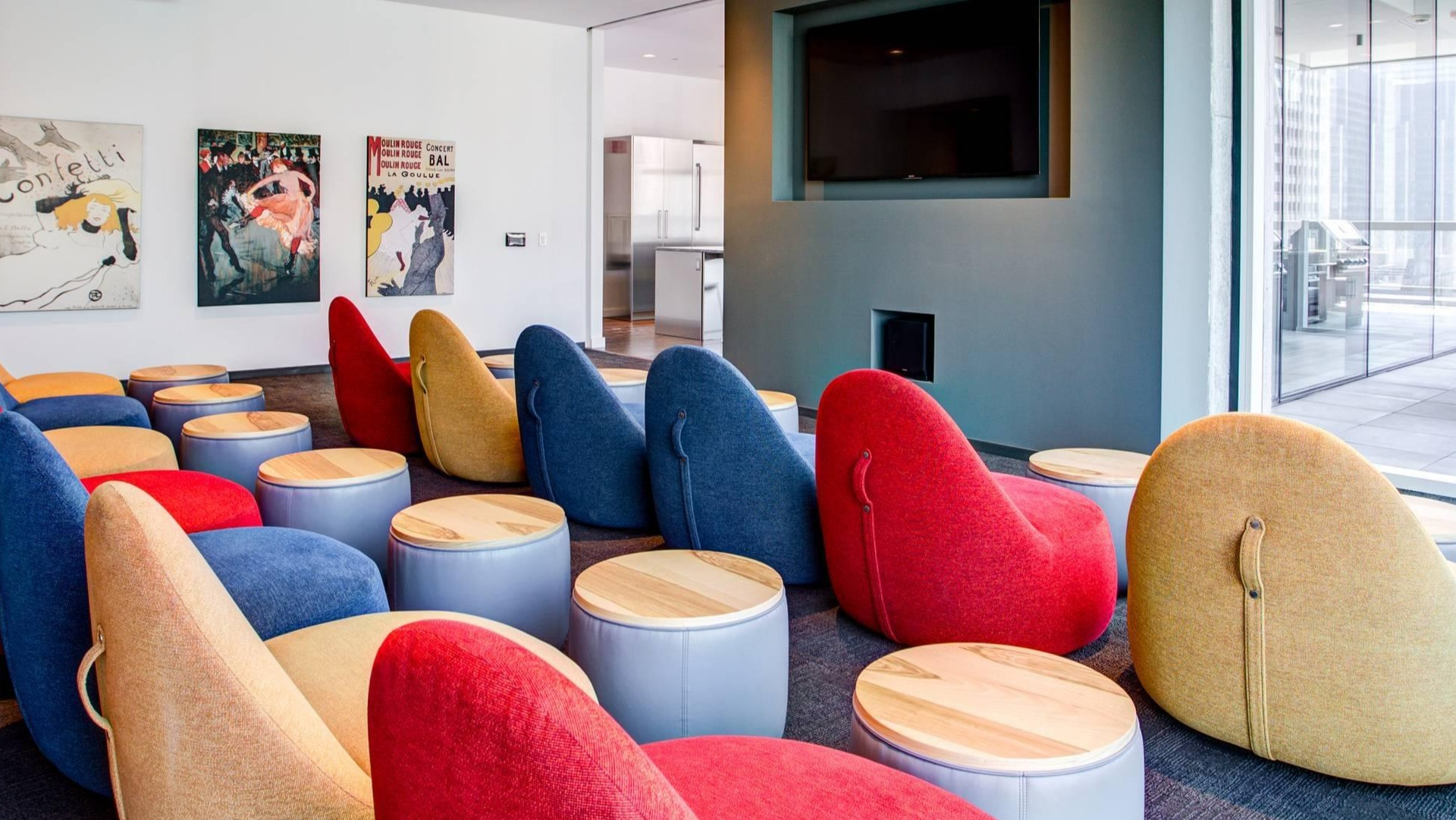 Colorful screening room with plush lounge chairs, personal side tables, and a large wall-mounted TV at Optima Signature apartments in Chicago