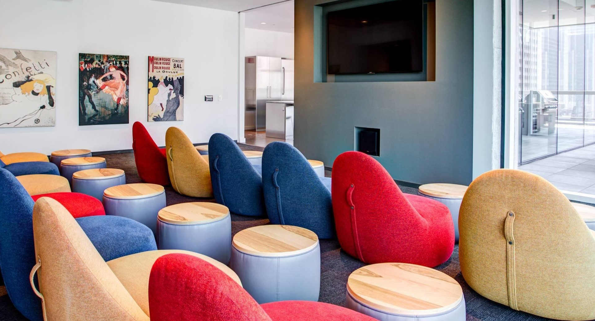 Colorful screening room with plush lounge chairs, personal side tables, and a large wall-mounted TV at Optima Signature apartments in Chicago