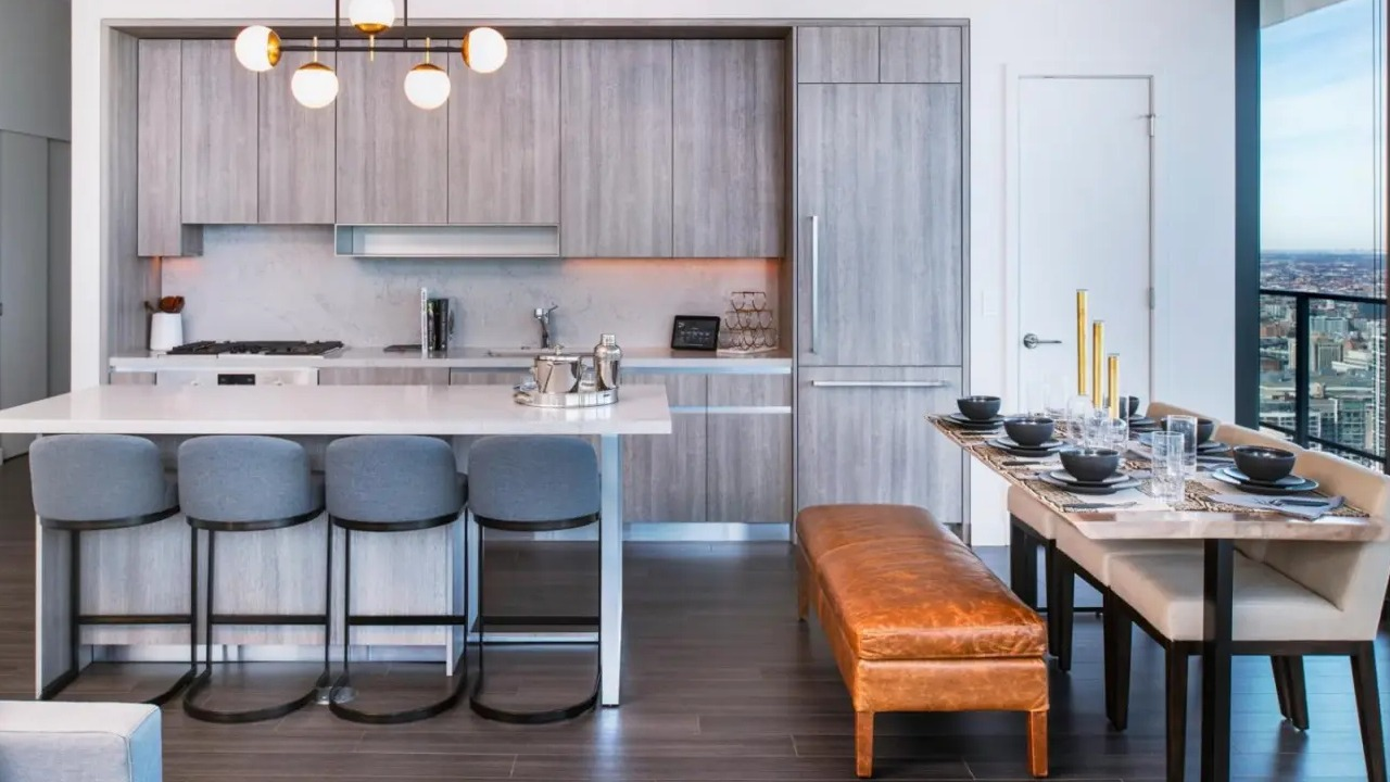 Modern apartment kitchen and dining area at NEMA Chicago, featuring grey cabinetry, a spacious island with seating, and elegant pendant lights