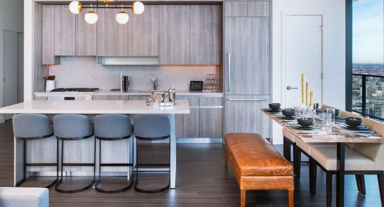 Modern apartment kitchen and dining area at NEMA Chicago, featuring grey cabinetry, a spacious island with seating, and elegant pendant lights