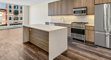 Spacious apartment kitchen at Nevele22 in Chicago, featuring a large island with a waterfall countertop, wood cabinetry, and stainless steel appliances