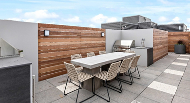 Modern outdoor kitchen and dining area at Nevele22 in Chicago, featuring built-in grills, a large table, and stylish privacy screens